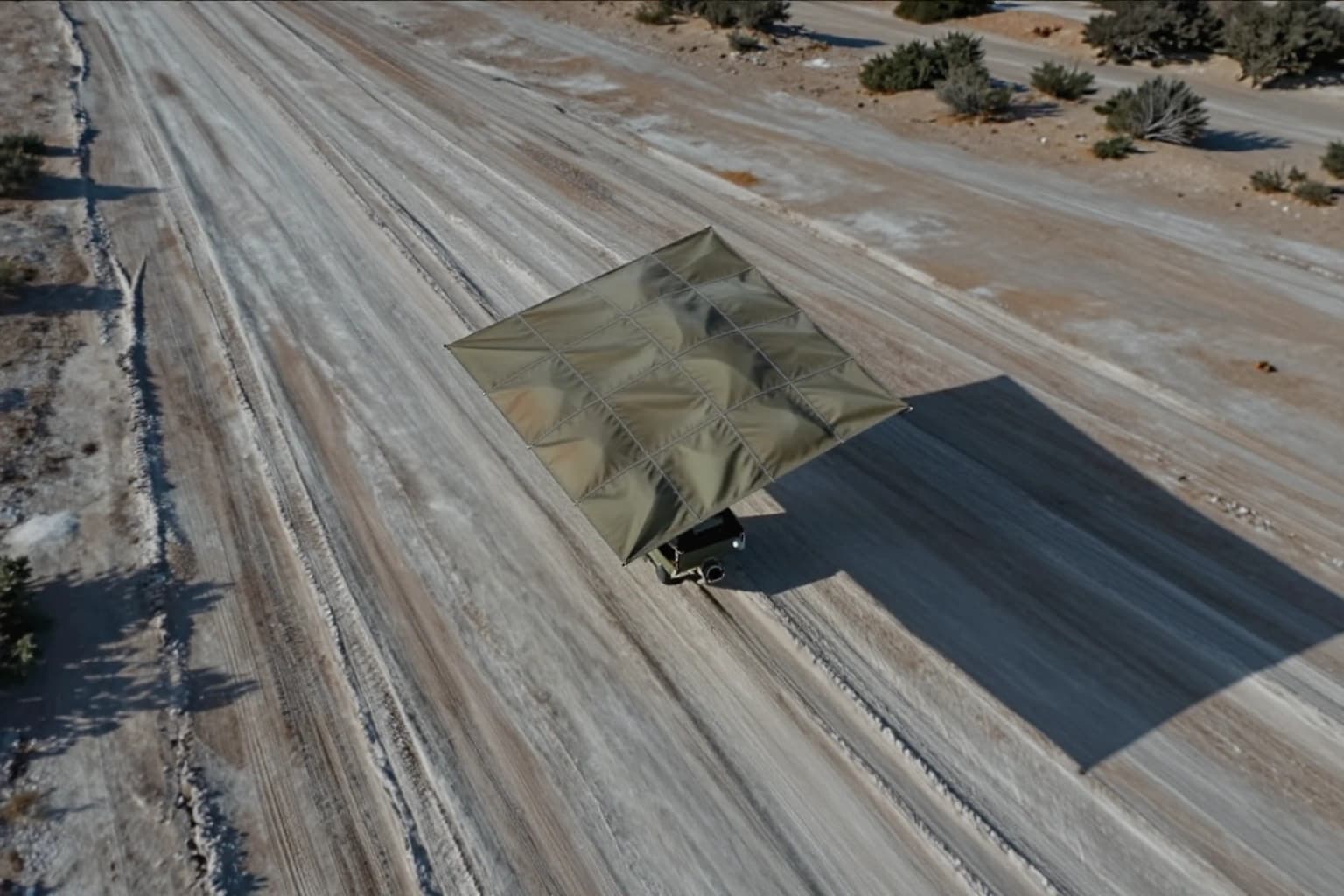 Air Cover camouflage deployed above a vehicle on an open salt-flat route